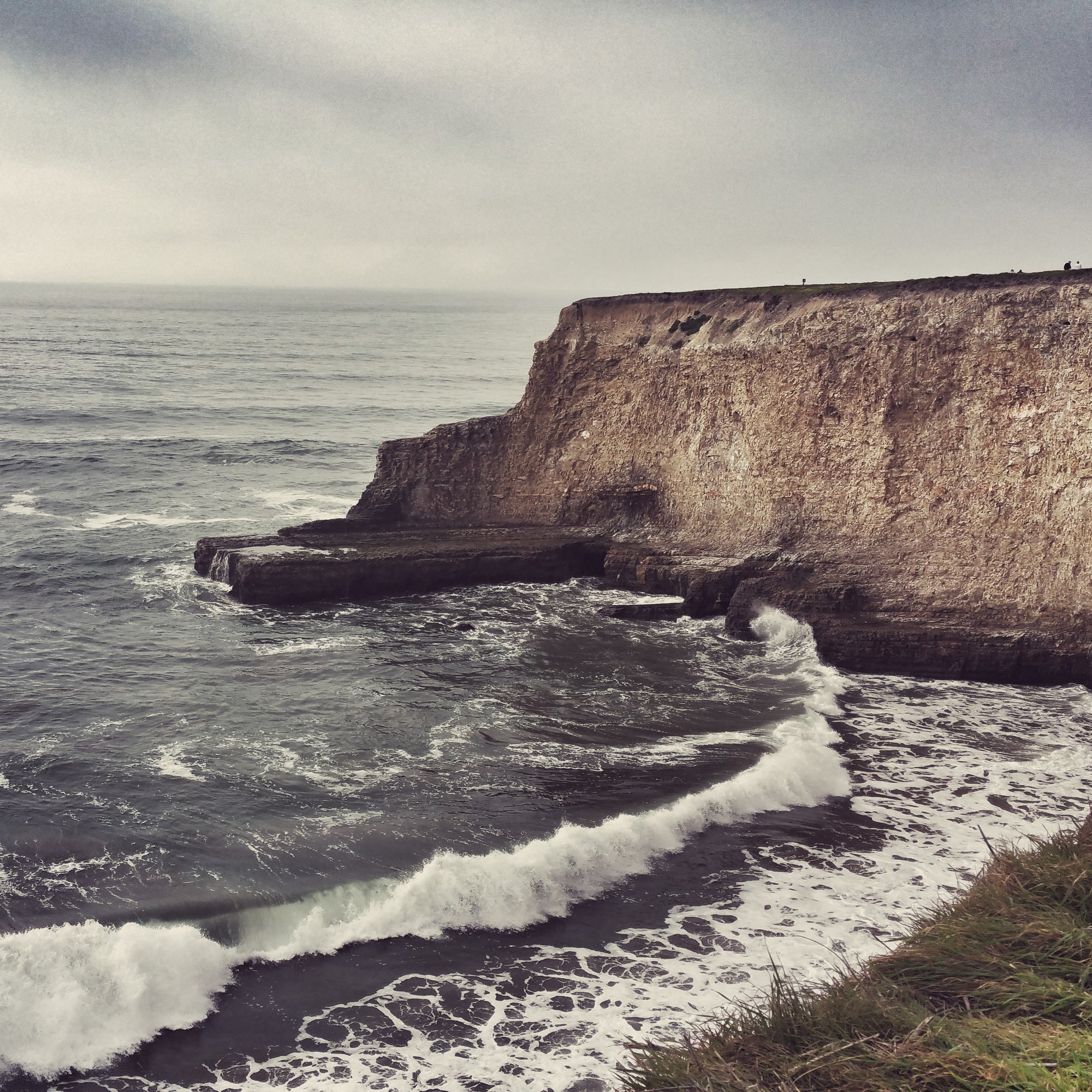 Cliffs with ocean waves crashing against them on a cloudy day in Davenport, CA