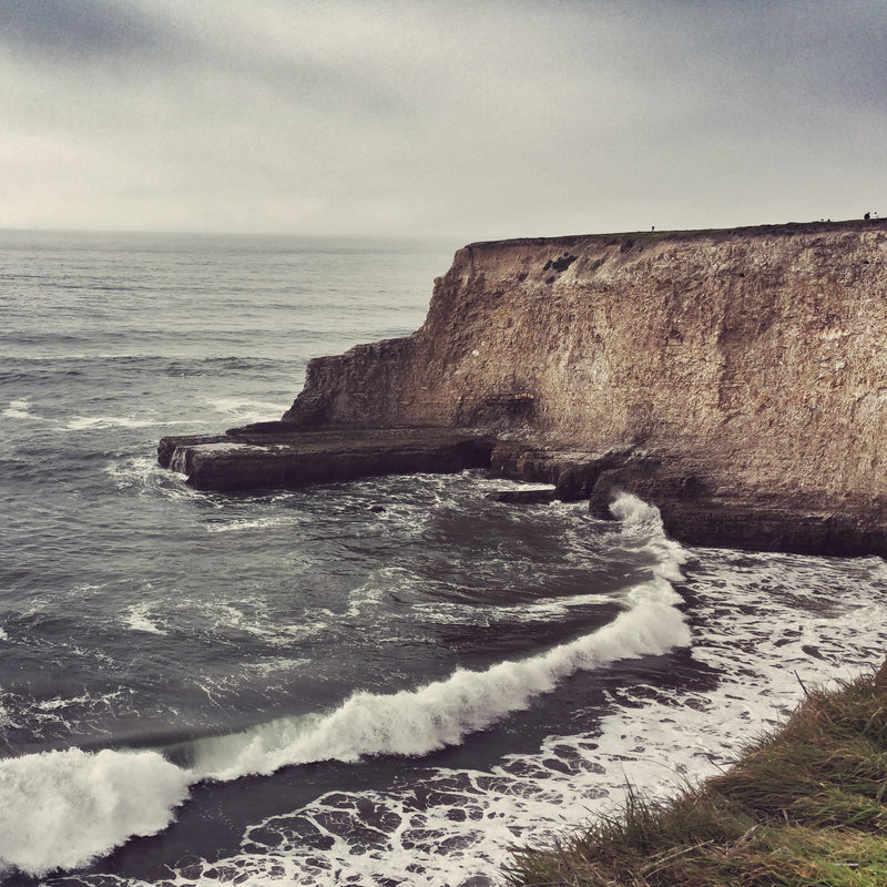 Cliffs with ocean waves crashing against them on a cloudy day in Davenport, CA