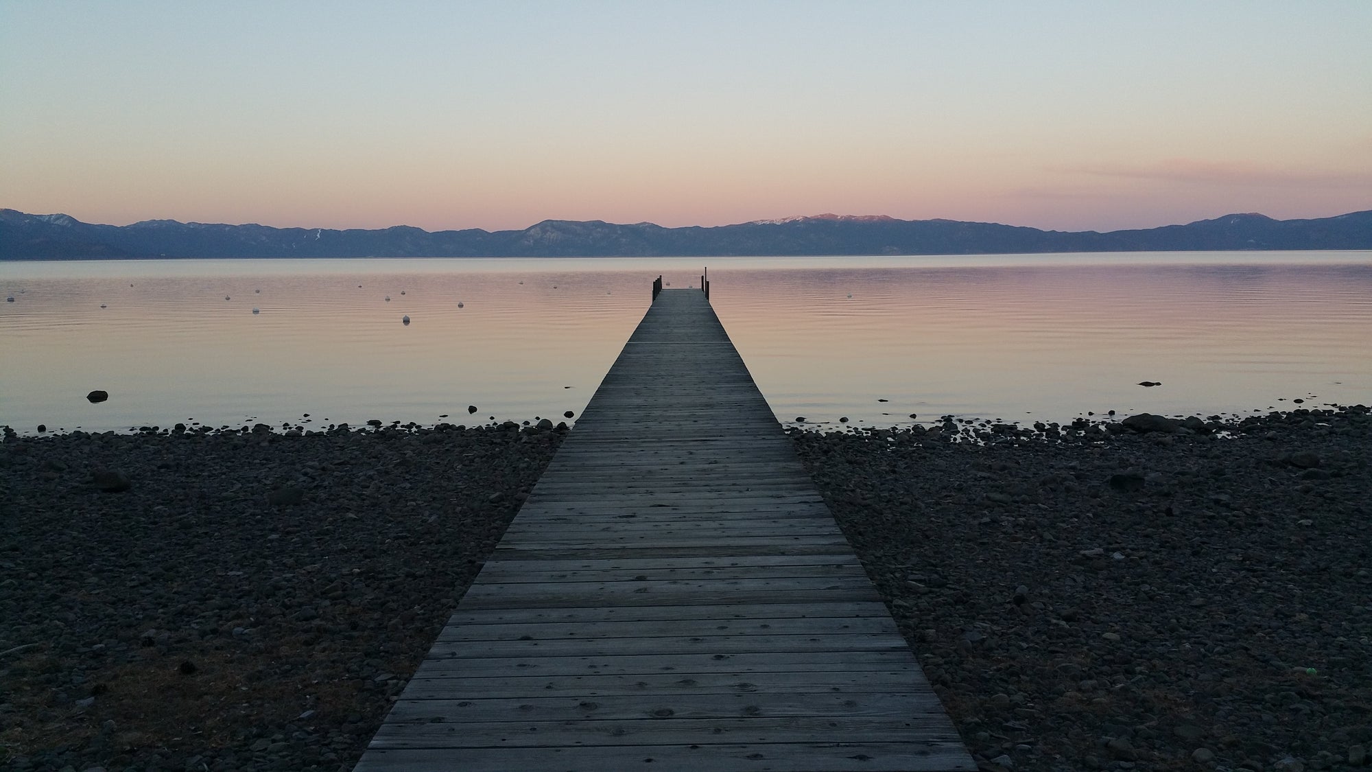 Wooden dock extending into a lake with mountains in the distance during sunset in Lake Tahoe, CA