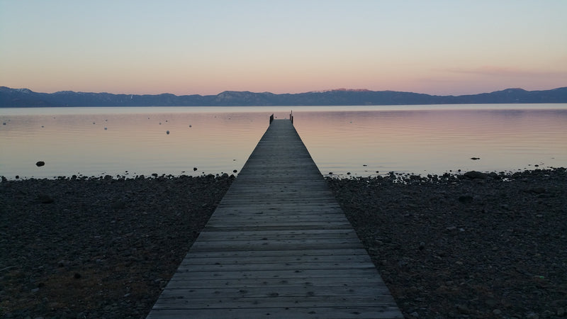 Wooden dock extending into a lake with mountains in the distance during sunset in Lake Tahoe, CA