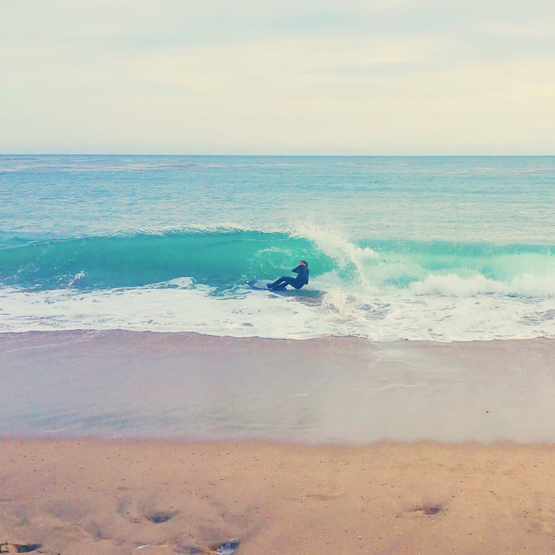 Person skimboarding on a wave at the beach in Santa Cruz, CA