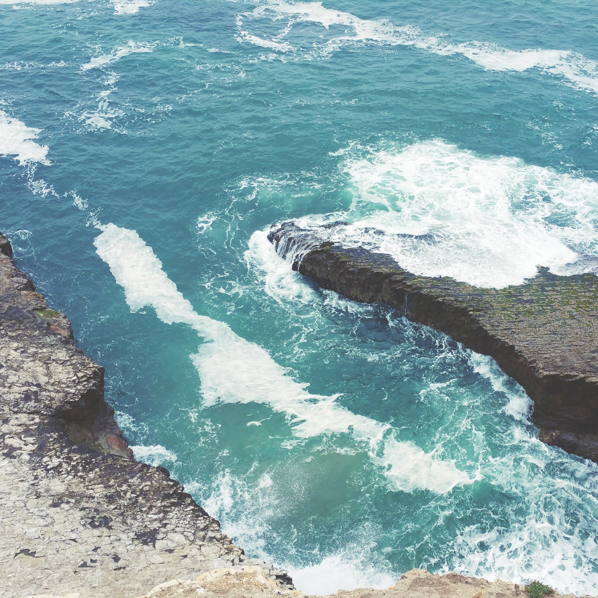 Turquoise ocean water crashing against a rocky cliff in Davenport, CA