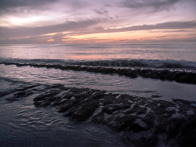 Sunset over a beach with wet sand and rocks in Sandy Beach, Puerto Rico